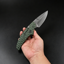 A hand holding an open folding knife with an olive green textured handle and a silver stonewashed blade, displayed against a dark background.