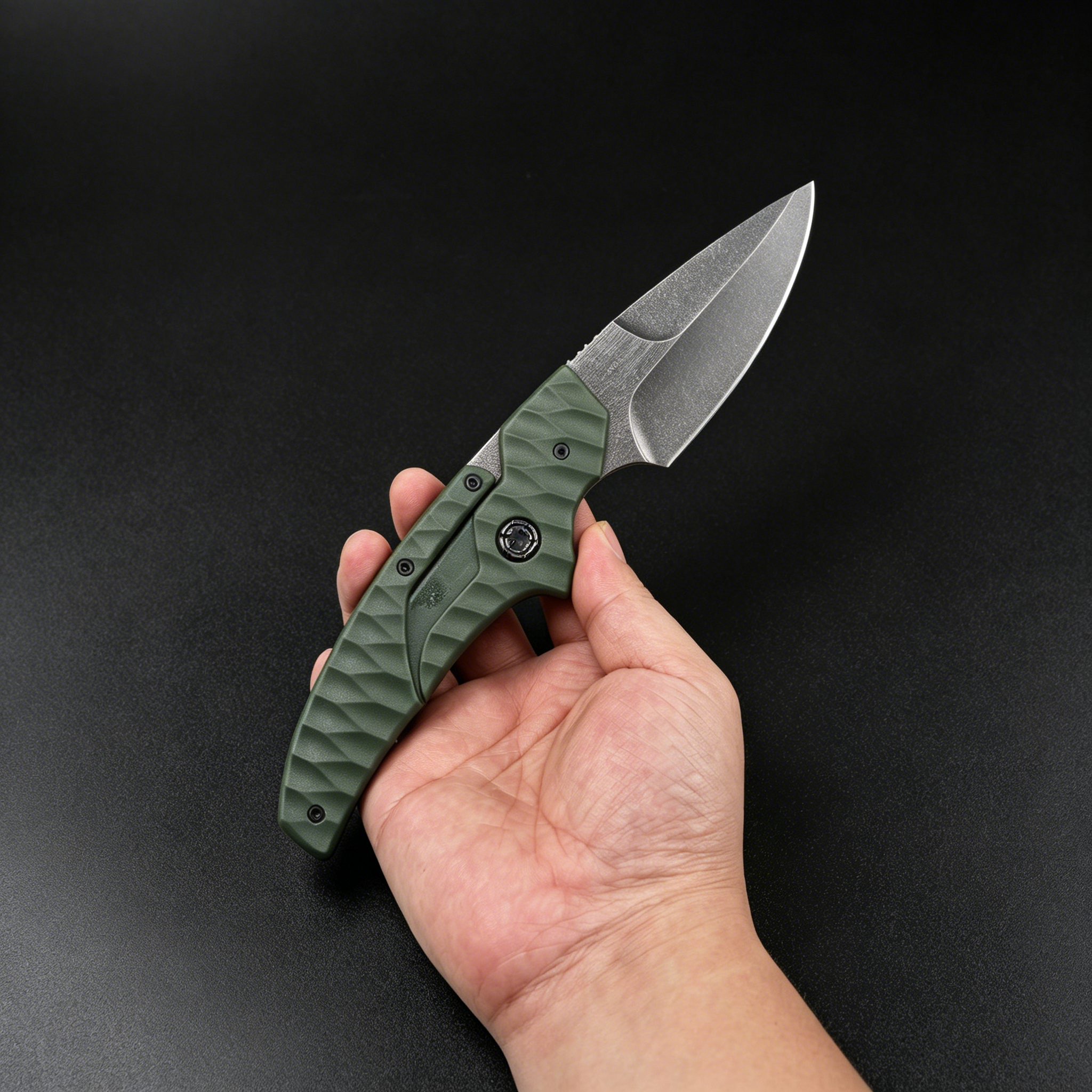 A hand holding an open folding knife with an olive green textured handle and a silver stonewashed blade, displayed against a dark background.