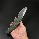 A hand holding an open Kizer folding knife with an olive green textured handle and a silver stonewashed blade, displayed against a dark background.