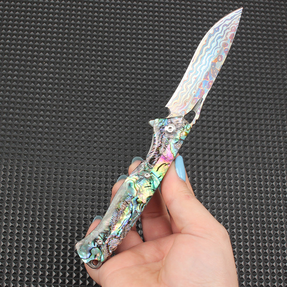 Display of this abalone handle folding knife fully opened in hand, with the colorful Damascus steel blade perfectly complementing the iridescent shell handle, offering both practical cutting capability and artistic aesthetics.
