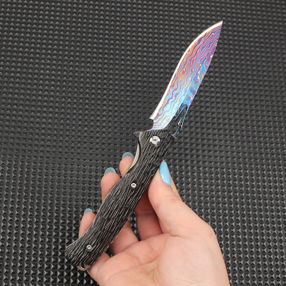Close-up of the fully opened folding knife, featuring a stunning colorful Damascus blade paired with a dark textured handle, showcasing premium EDC knife aesthetics.