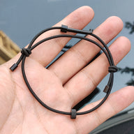 A close-up of a hand holding a black tactical handcuff key, highlighting the cord design, metal key insert, and adjustable bead, against a dark background.