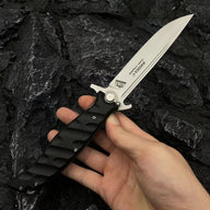 A hand holding an open Noks folding knife with a silver blade and black handle, displayed on a dark rocky background.