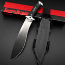 A Kershaw fixed blade knife with a black blade and textured handle, silver accents, displayed next to its black molded sheath and red packaging box on a dark background.