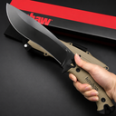 A hand holding a Kershaw fixed blade knife with a tan textured handle and black blade, displayed above a tan sheath and red packaging box on a dark background.