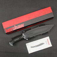 A sheathed Kershaw fixed blade knife with a black handle, displayed with its red and black packaging box and product manual on a dark textured surface.
