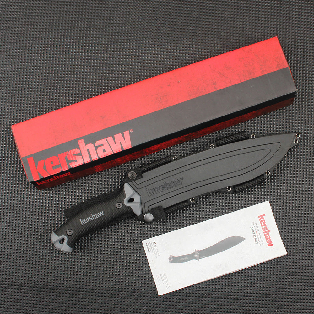 A sheathed Kershaw fixed blade knife with a black handle, displayed with its red and black packaging box and product manual on a dark textured surface.
