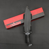 A sheathed Kershaw fixed blade knife with a black handle resting vertically on a red and black Kershaw packaging box, displayed on a dark gray textured surface.