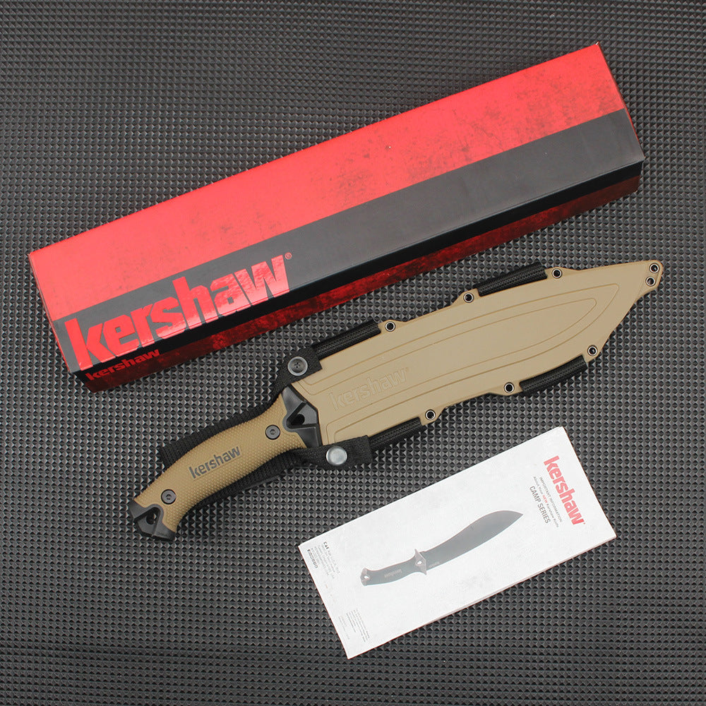 A sheathed Kershaw fixed blade knife with a tan handle and molded sheath, displayed with a red and black packaging box and a product manual on a dark textured surface.