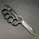 A view of the backside of a black knuckle duster folding knife, showing the textured inner holes of the knuckle guard and a black blade, on a carbon fiber background.