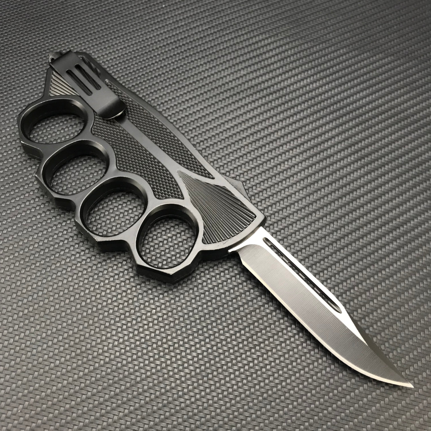 A view of the backside of a black knuckle duster folding knife, showing the textured inner holes of the knuckle guard and a black blade, on a carbon fiber background.