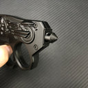 A close-up of the threaded glass breaker tip on a black knuckle duster folding knife, held by a hand, displayed on a carbon fiber background.
