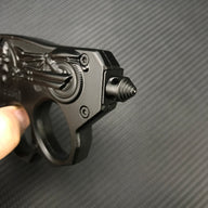 A close-up of the threaded glass breaker tip on a black knuckle duster folding knife, held by a hand, displayed on a carbon fiber background.