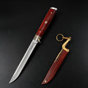 An open M390 folding knife with a wood handle and metal guard, positioned next to its separate wooden sheath with a brass linkage and key ring, on a dark background.