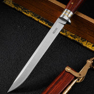 A close-up of a folding knife featuring an M390 steel blade, a wood handle, and silver and brass metal guards, displayed on a dark textured surface.