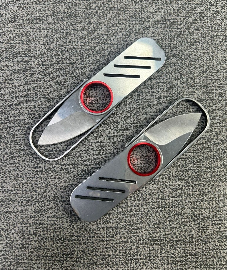An open and a closed silver metal keychain folding knife lying flat on a grey textured surface, highlighting the ultra-thin design.