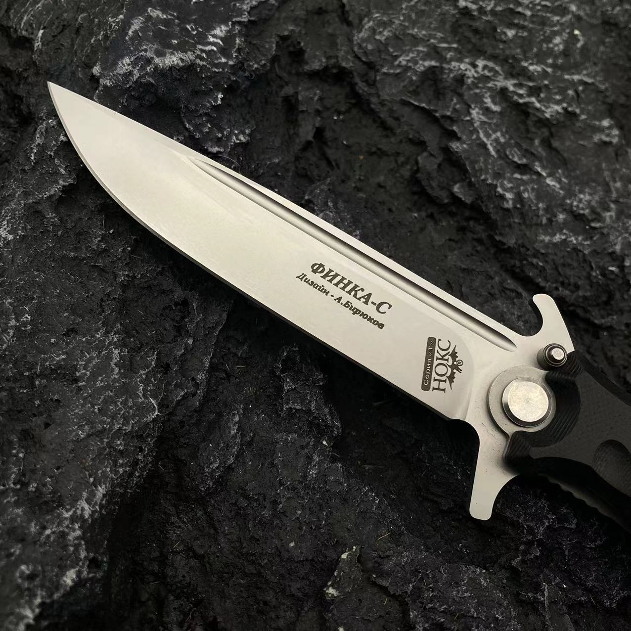 A close-up of the silver blade of a Noks folding knife, clearly showing the Cyrillic engraving and brand logo.