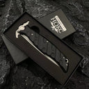 A Noks folding knife resting inside its black presentation box, displayed on a dark rocky background.