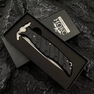 A Noks folding knife resting inside its black presentation box, displayed on a dark rocky background.