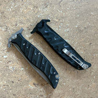 Two closed Noks folding knives with black handles and silver pocket clips, displayed on a light wooden background.