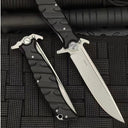 An open and a closed Noks folding knife on a black rope-textured surface, showing the D2 steel marking on the open blade.