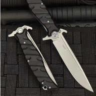 An open and a closed Noks folding knife on a black rope-textured surface, showing the D2 steel marking on the open blade.