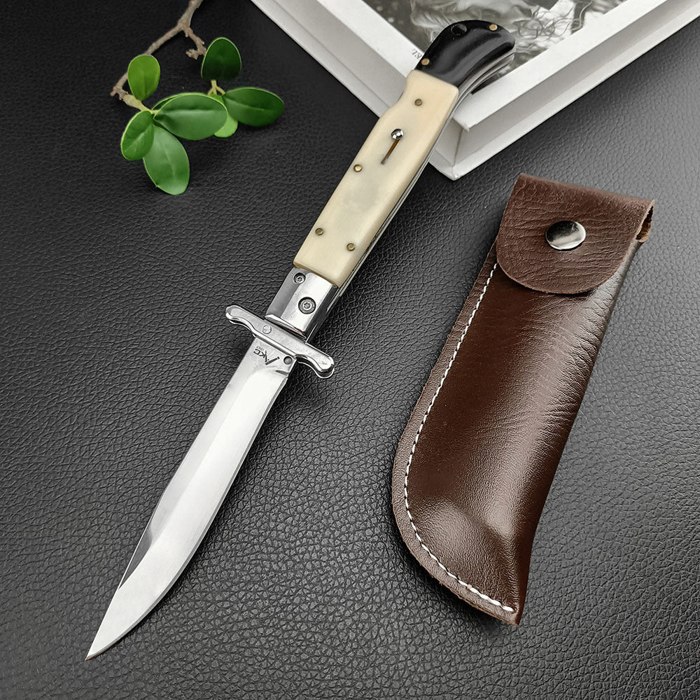 An open Italian stiletto knife with a cream bone handle and silver blade, displayed next to a brown leather sheath on a dark textured surface.