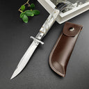 An open Italian stiletto knife with a white pearl handle and silver blade, displayed next to a brown leather sheath with white stitching on a dark textured surface.