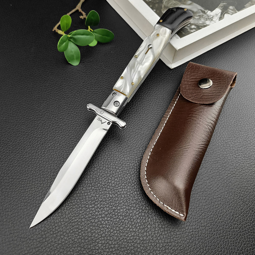 An open Italian stiletto knife with a white pearl handle and silver blade, displayed next to a brown leather sheath with white stitching on a dark textured surface.