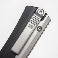 A close-up of a silver pocket clip on a black out-the-front knife, showing engraved text and serial numbers on a white background.