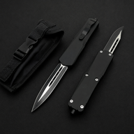 Two black OTF knives with carbon fiber handles and silver blades, displayed next to a black nylon sheath.