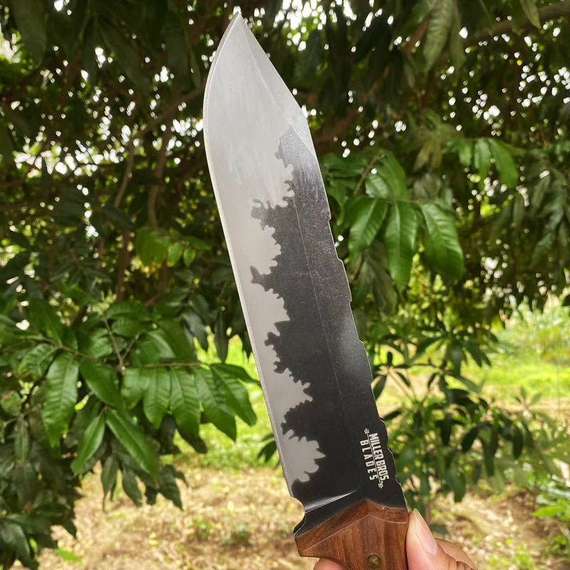 Alt Text: A close-up of a fixed blade knife with a hammered blade and wooden handle held in front of green tree leaves outdoors.