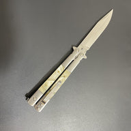 A close-up of an open balisong butterfly knife with a pearl handle and a silver blade, displayed diagonally on a dark background.