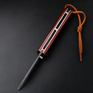 A closed EDC folding knife with a polished red wood handle and a slender blade profile, featuring a brown leather lanyard and silver liners, displayed on a dark textured background.