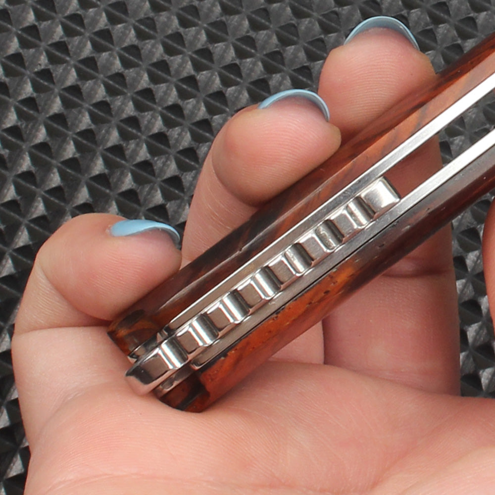 Close-up of the folding knife's side structure, clearly showing the thickness of the redwood handle, the flipper tab profile, and the internal bearing system ensuring smooth deployment and closing.