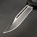 A close-up of a silver folding knife blade showing a central groove and a brushed metal finish, displayed on a textured dark background.