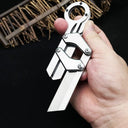 A hand holding a silver folding knife with a ring handle and mechanical linkage design, displayed on a dark background with textured details.
