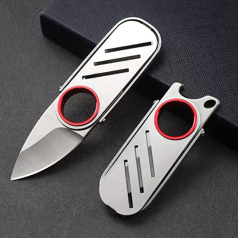 An open and a closed folding keychain knife with a red circular ring and silver steel body, resting on a black fabric surface.