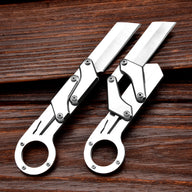 Two silver mechanical folding knives with ring handles and grooved blades, one fully opened and one partially folded to show the linkage mechanism, displayed on a dark wooden background.