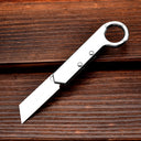 An open silver folding knife with a ring handle, resting on a dark textured wooden background.