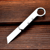 An open silver folding knife with a ring handle, resting on a dark textured wooden background.