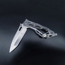 A partially folded silver skeletonized tactical knife, showing the folding mechanism and the Tanto blade profile, displayed on a dark background.