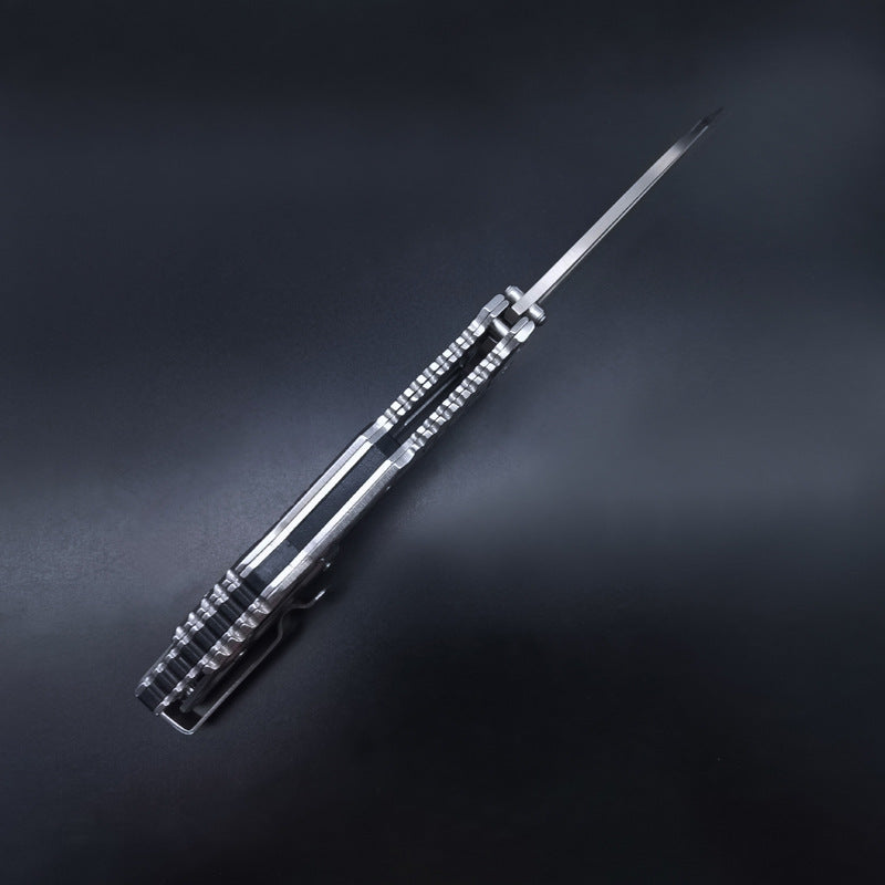 A side spine view of a silver skeletonized folding knife, showing the grooved blade spine and the intricate handle structure, displayed on a dark background.