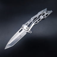 An open tactical folding knife with a silver Tanto blade and a skeletonized metal handle, displayed on a dark background.