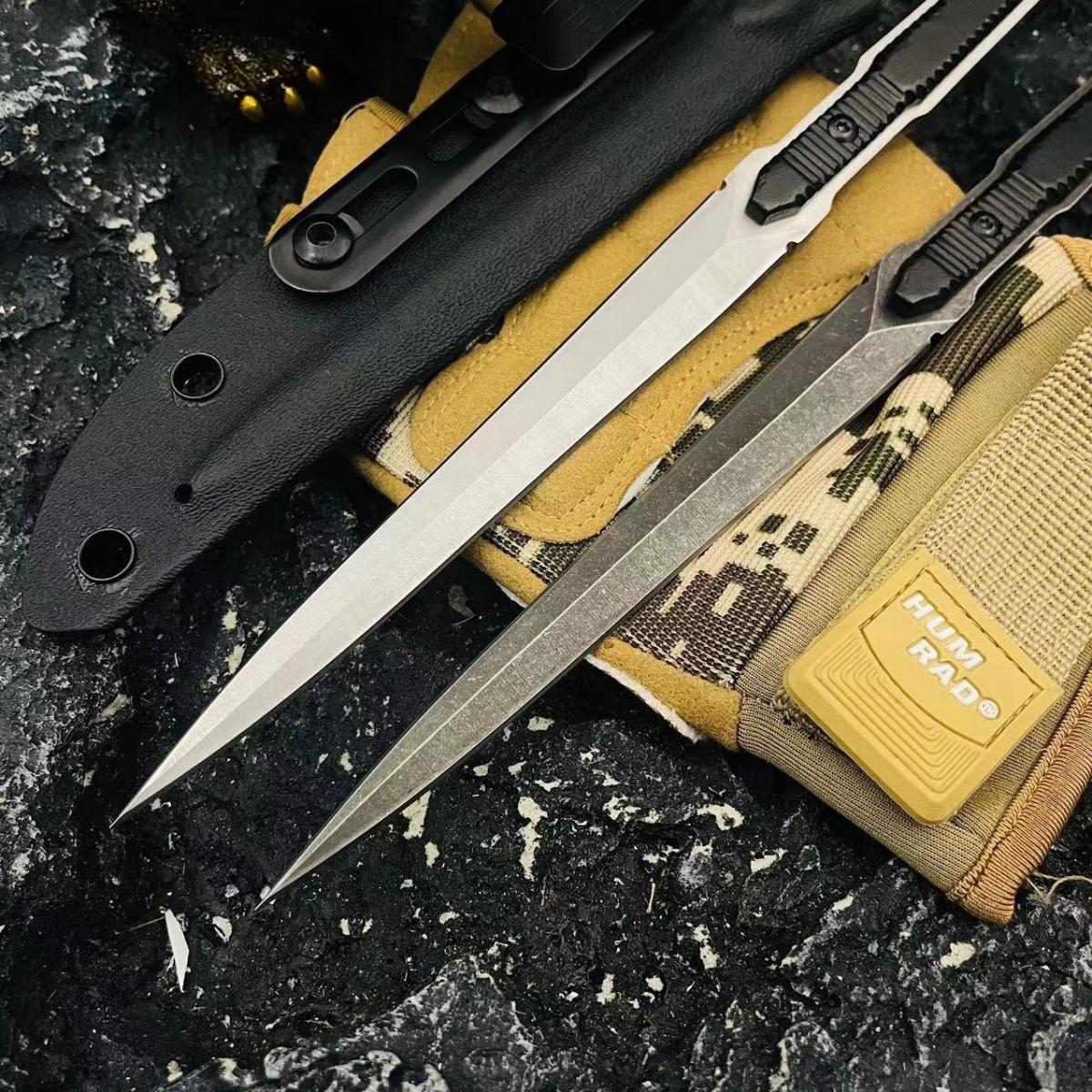Two slim folding knives, one silver and one black, laid over a black sheath and a digital camo pouch against a rough rocky surface.