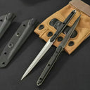 Two open slim tactical folding knives, one with a silver blade and one with a black blade, displayed next to tan tactical gloves and black sheaths on a dark background.