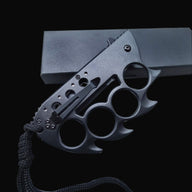 A closed black Tac-Force folding knife with a knuckle duster handle, black pocket clip, and lanyard, displayed on a dark background.