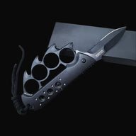 An open black Tac-Force knuckle duster folding knife with a partially serrated blade, silver logo, and black braided lanyard, displayed on a dark box against a dark background.