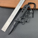 An open black Tac-Force folding knife with a knuckle duster handle and serrated blade, displayed with a ruler on a carbon fiber textured background.
