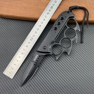 An open black Tac-Force folding knife with a knuckle duster handle and serrated blade, displayed with a ruler on a carbon fiber textured background.